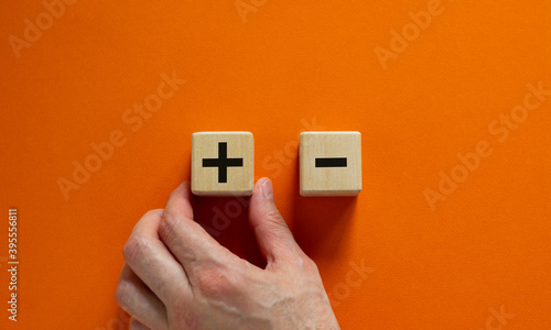 Plus or minus. Businessman holds a cubes with plus icon. Wooden cube with minus icon. Beautiful orange background. Copy space. Business and plus and minus concept.