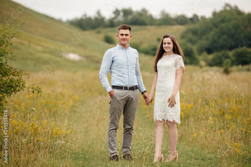 Young beautiful couple hand by hand walking in the field in summer. woman with long hair and man with stylish haircut. © Andriy Medvediuk