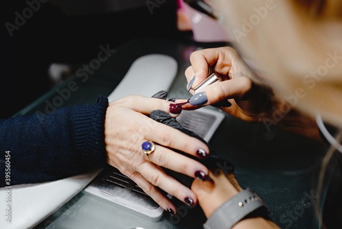 Close up with unrecognizable hands of manicurist applying red gel polish on client s nails. professional  beauty concept.