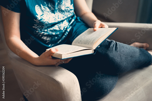 A young pretty woman sits on an armchair and reads a book.Close-up of female hands holding an open book. Cozy home © Peter Rusinov