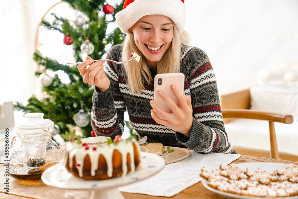 Positive girl in christmas santa hat eating cake Positive girl in christmas santa hat eating cake
