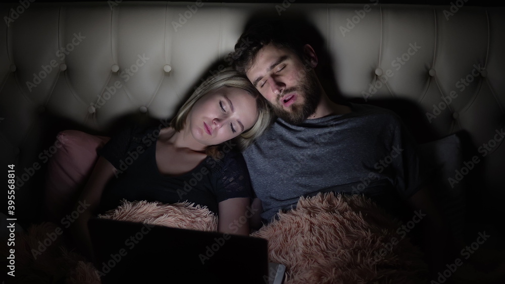 A man and a woman, a young couple watched a movie in bed and fell asleep before the laptop A man and a woman, a young couple watched a movie in bed and fell asleep before the laptop