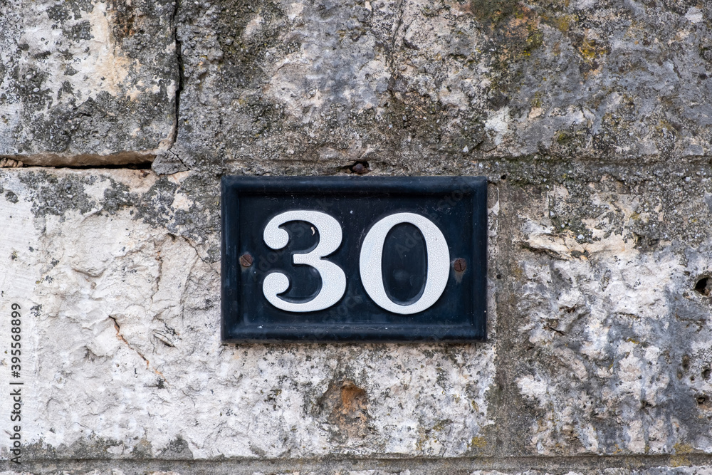 Street number 30. House address metal sign on stone wall. Street number 30. House address metal sign on stone wall.