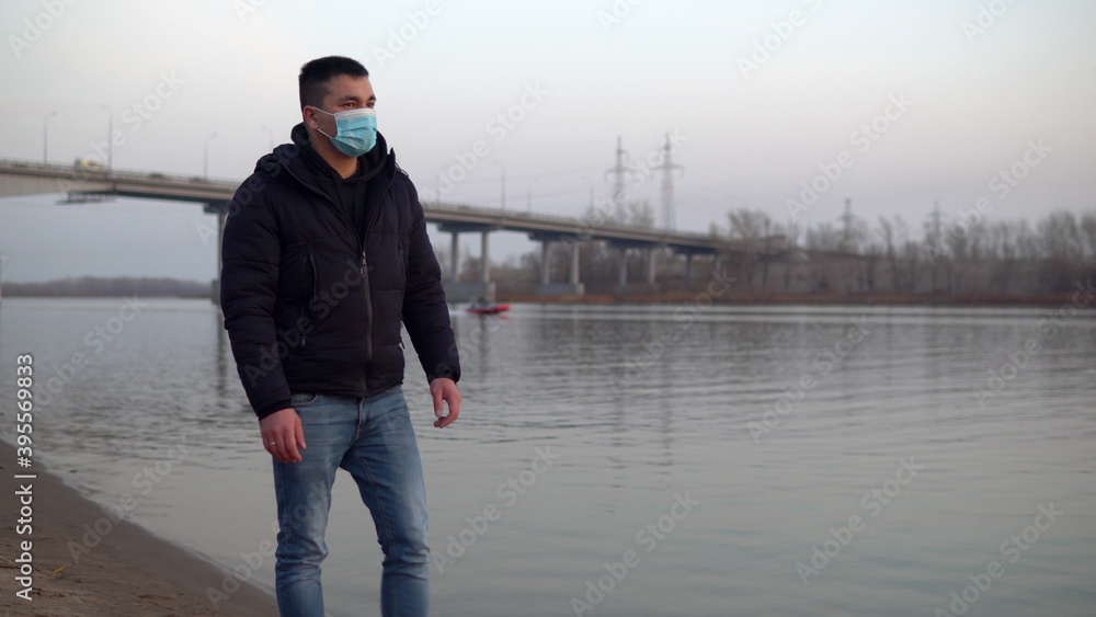 A man in a mask on his face walks along the river bank