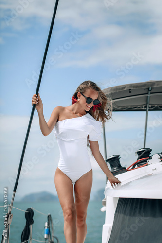 portrait of happy pretty girl with white swimsuit, black sunglass and long curly blonde hair standing on yacht at summertime. looking at camera with toothy smile.. © Semachkovsky 