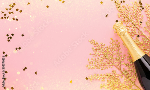 Bottle of champagne wine golden shiny confetti branches pastel pink background