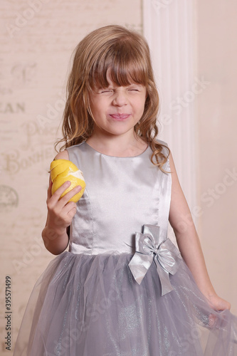cute little blond baby girl eating sore lemon and grimacing on retro wall interior background