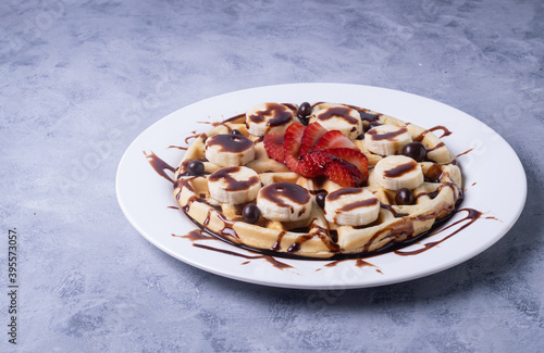 Delicious Belgium waffles with chocolate, bananas, and strawberries on a plate on the table photo