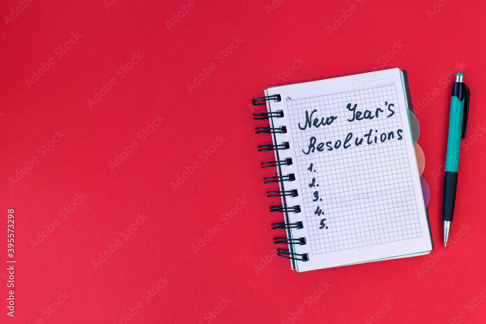Writing in a notebook New Year's resolutions on red background. New Year's resolutions concept. Flat lay. Writing in a notebook New Year's resolutions on red background. New Year's resolutions concept. Flat lay.