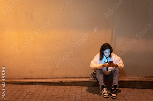 Schilderij op canvas Beautiful young woman using her phone sitting in the night city street waiting for someone