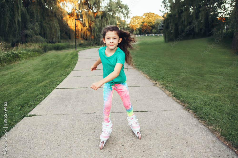 Happy Caucasian girl riding in roller skates on road in park on summer day. Seasonal outdoors children activity sport. Healthy childhood lifestyle. Kids individual summer sport.