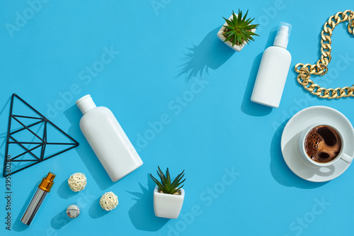 White flask and pump bottle with no label, cup of coffee, chain, figurine of triangle, perfume container on blue background. Close up, copy space