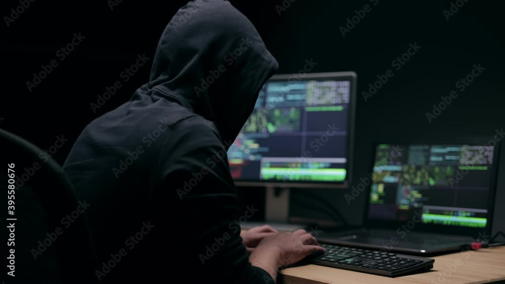 Unknown man in hood typing on keyboard in darkness, illegal activity, business espionage Unknown man in hood typing on keyboard in darkness, illegal activity, business espionage
