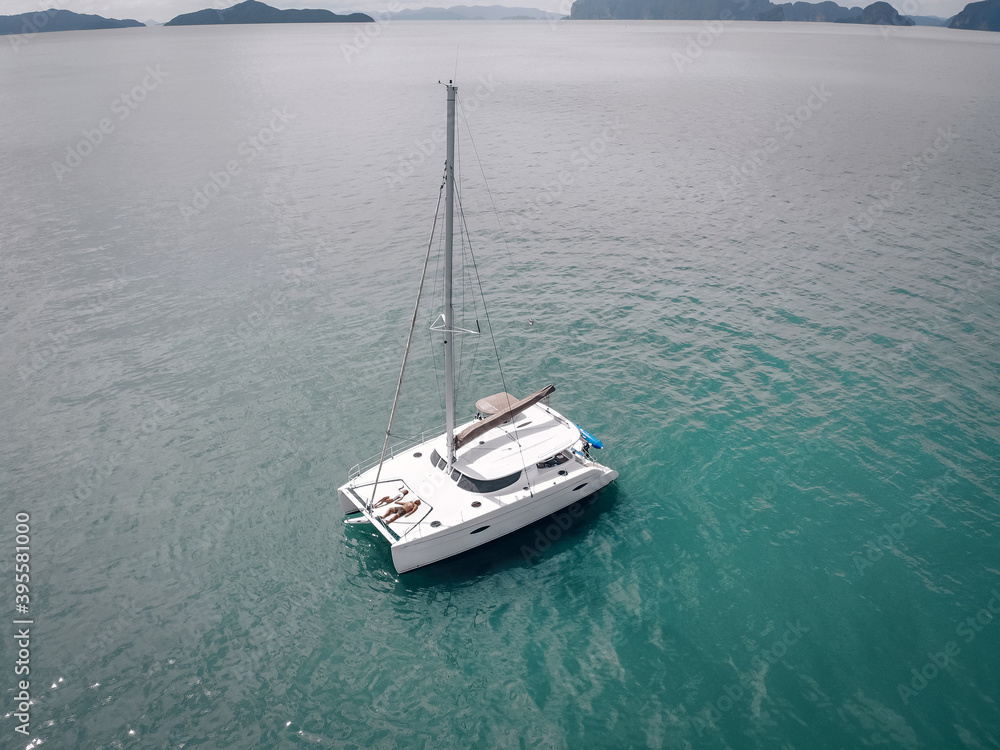 Naklejka premium Young couple relaxing on board of the sail boat anchored in shallow tropical bay. Aerial photo