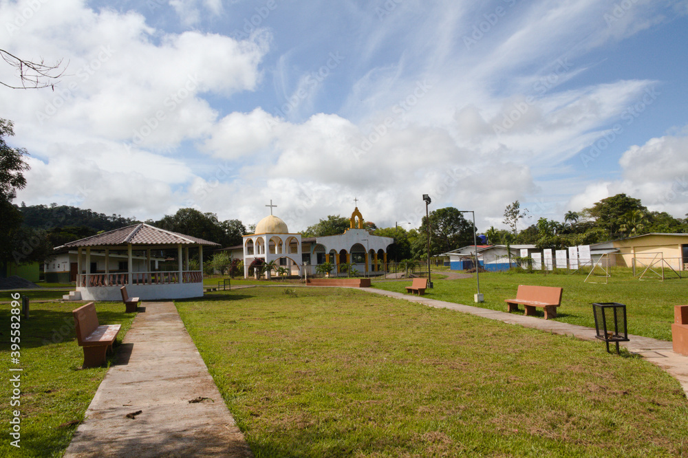 village park with green areas, kiosk and church on a sunny day