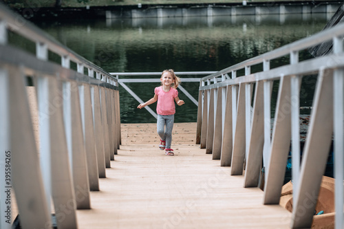 Smiling little caucasian kid girl in pink t-shirt and blue jeans running up metal stair. - Image