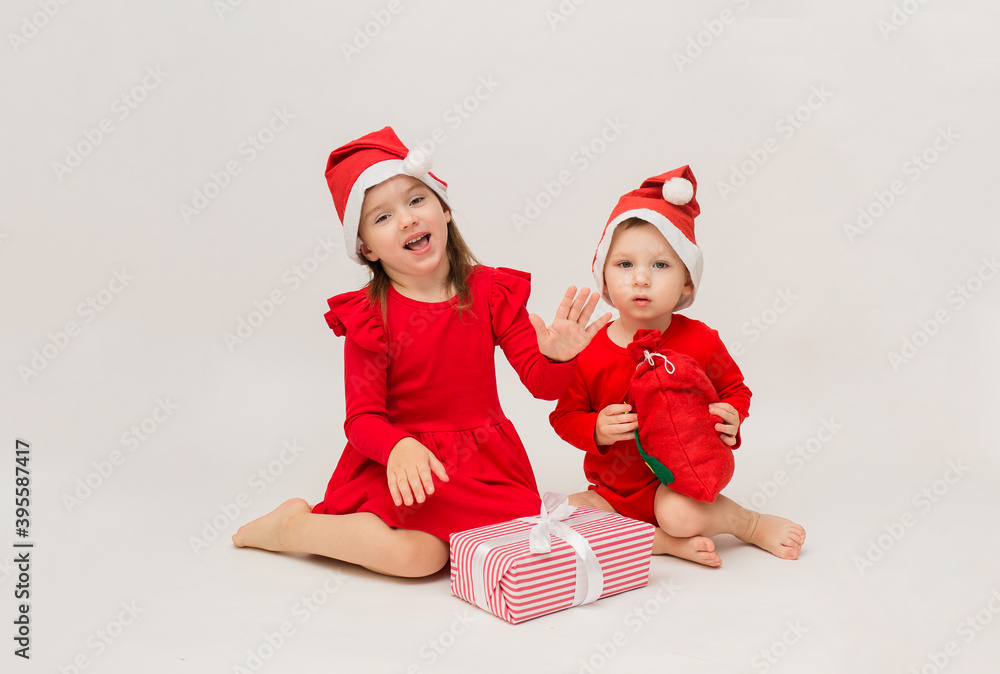 Obraz premium happy little girl and boy in red caps with Christmas gifts on white background with space for text