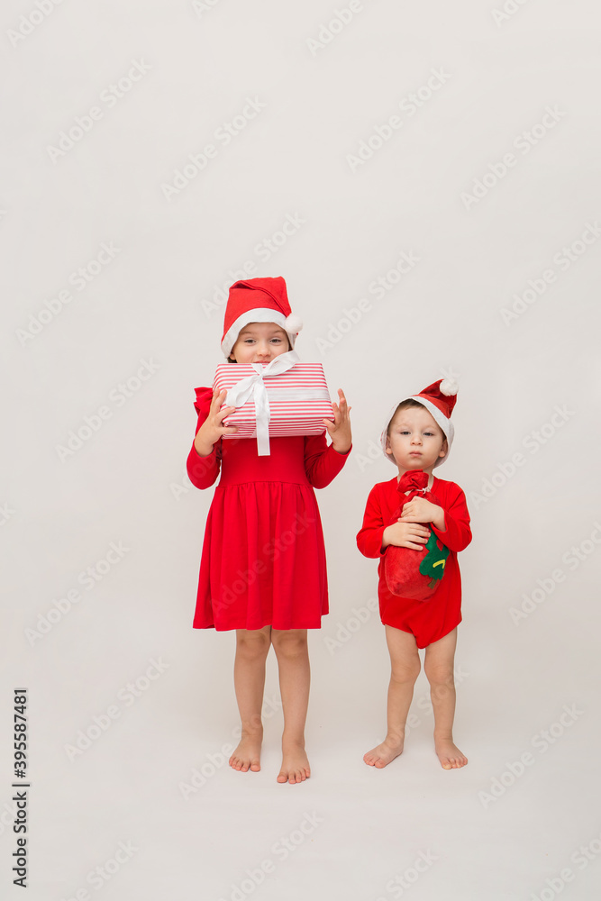 Obraz premium a little girl and a full-length boy in red caps with Christmas gifts on a white background with a copy of the space