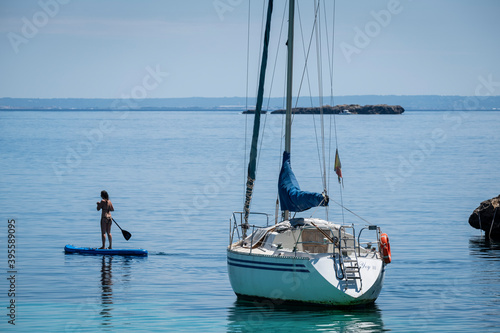 young woman practicing paddle surf next to a sailboat, Cala Portals Vells, Calvia, Mallorca, Balearic Islands, Spain © Tolo