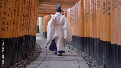 Japanese buddhist man walking along a path lined with Torii Gates in Fushimi Inari Shrine temple, Kyoto, Japan. photo