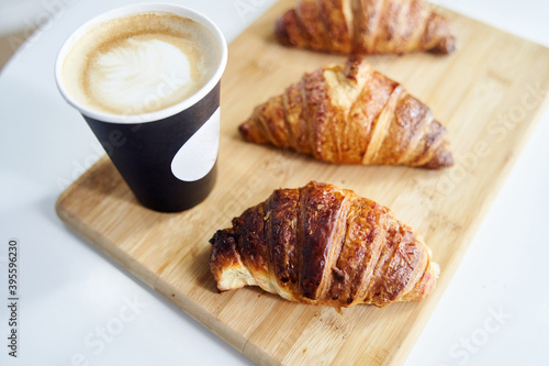 Golden fresh croissants with coffee on a wooden tray close up