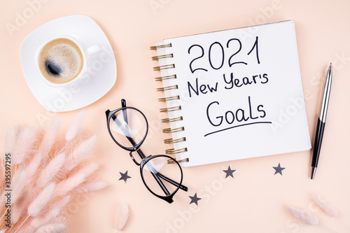 New year 2021 goals on desk. 2021 goals with open notebook, coffee cup, eyeglasses, flowers on pastel background. Resolutions, goals, plan, strategy, feminine, idea concept. New Year 2021 template