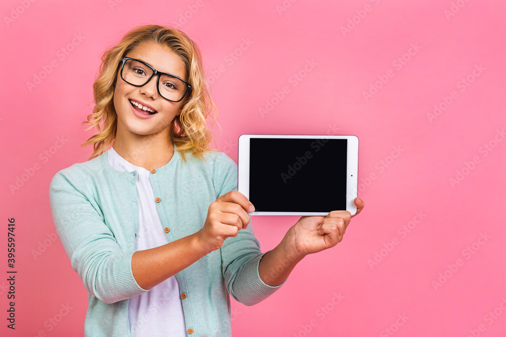 Happy attractive little kid teen girl holding a blank tablet in her hands so that the blank screen with white copyspace. Isolated over pink background. Happy attractive little kid teen girl holding a blank tablet in her hands so that the blank screen with white copyspace. Isolated over pink background.