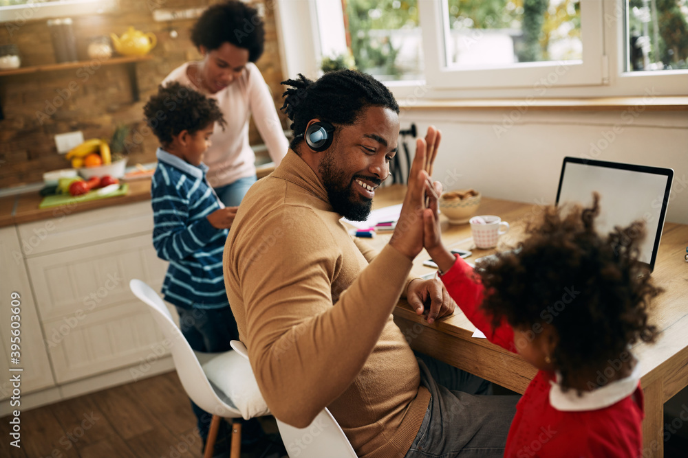 Happy black father giving high-five to his daughter while working at home.