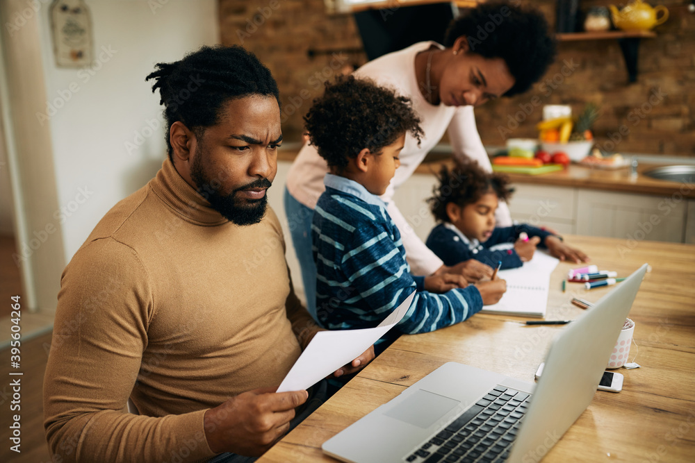 Black father working on laptop while mother is homeschooling their kids. Black father working on laptop while mother is homeschooling their kids.
