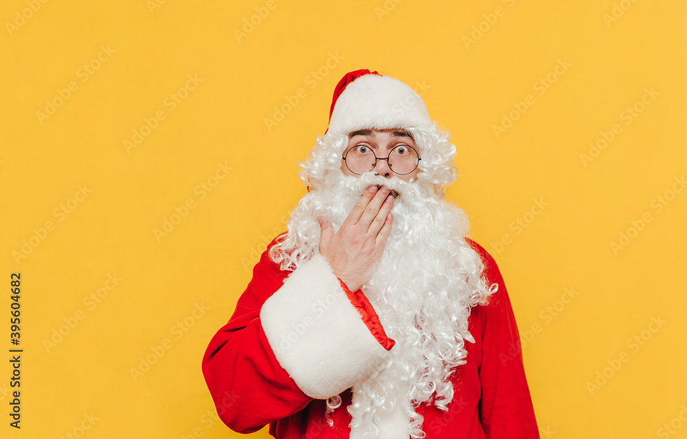Surprised Santa Claus is touching his mouth with his hand showing an amazement gesture, feeling shocked, looking at the camera with his scared eyes wide open. Surprised Santa Claus is touching his mouth with his hand showing an amazement gesture, feeling shocked, looking at the camera with his scared eyes wide open.