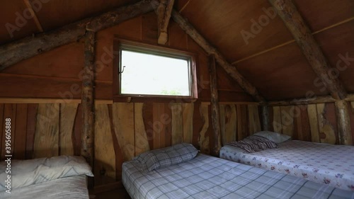 Inside the rustic bedroom of a mini house in the forest. Camera tilts towards the upwards from the mattresses on the floor to the small window. photo