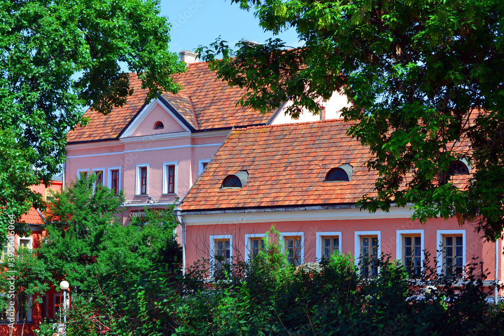 Facades of historic houses in Trinity Suburb or Trinity Hill (Trajeckaje pradmiescie) - the oldest surviving district of Minsk. Green trees on a foreground. Summertime in Republic of Belarus.