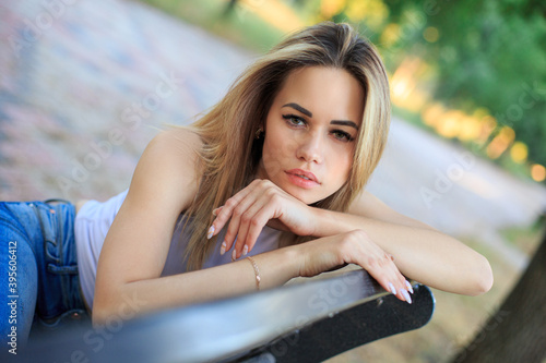 Portrait of a young blonde woman who rests on the back of the bench with her hands.