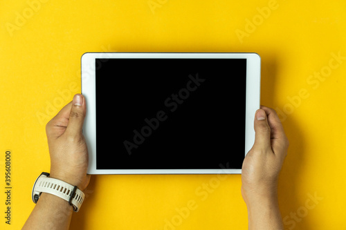 Table top view aerial image of accessories office desk background concept.Flat lay of Hand holding on white tablet on modern rustic yellow paper and space.