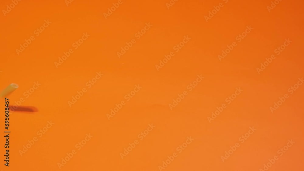 Dry uncooked penne pasta pieces fall down on orange background. Dry uncooked penne pasta pieces fall down on orange background.