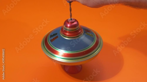 Multicolored metal spinning top or whirligig top is traditional toy for preschool childs. Rotates in circle on orange surface. photo