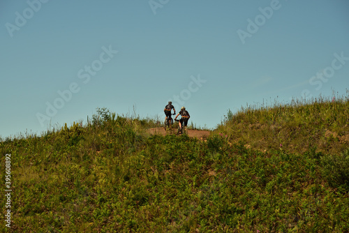 Two mountain bikers disappearing over a hill on a jeep track