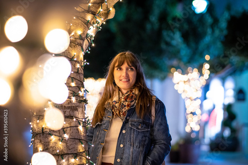 Close-up of young Spanish woman looking at christmas lights in outdoor mall, woman smiling, large bokeh of lights photo