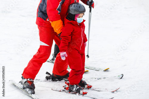 Portrait of a little girl skier in medical mask during COVID-19 coronavirus on a snowy mountain at a ski resort