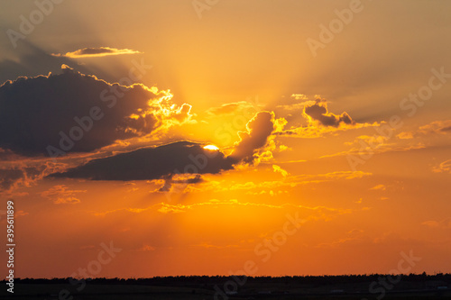 The sun hides behind the clouds at orange sunset sky above horizon. Abstract sunset background. Beauty in Nature theme.