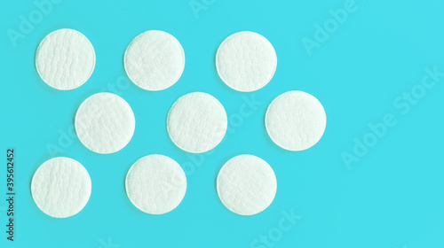 Nine white cotton cosmetic pads arranged on cyan blue board, closeup view from above