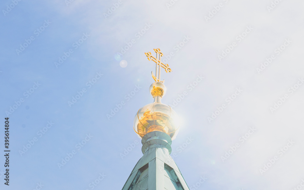 Golden dome and cross of the church against the blue sky, illuminated by the sun