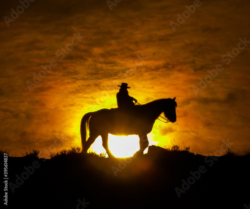 horse and rider cowboy silhouette at sunset western rider in western tack against red orange sky photo