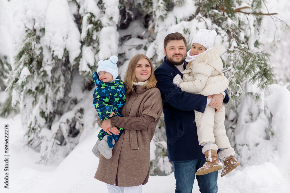 Fototapeta premium young Caucasian parents are holding children - a boy and a girl and hugging, looking at the camera in a snowy winter forest. Family winter vacation in nature 