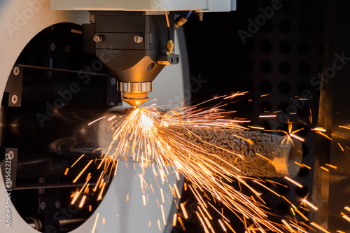 Metalworking, equipment, machining, industrial, technology, manufacturing concept. Automatic cnc laser cutting machine working with cylindrical metal workpiece with many sparks at factory, plant