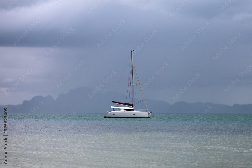 white yacht with sail set goes along the island on cloudy day. cloudy sky.