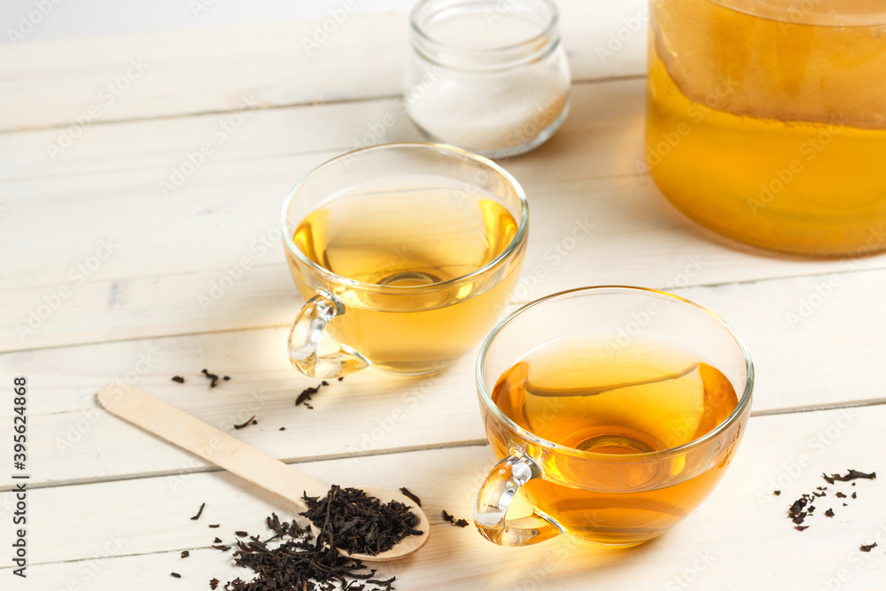 Two glass cups of Kombucha tea, a sweet and sour carbonated drink originally from China. On a light wooden background Two glass cups of Kombucha tea, a sweet and sour carbonated drink originally from China. On a light wooden background