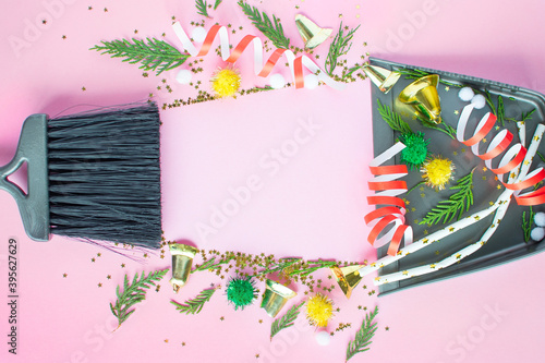 Christmas cleaning after the mess. Cleaning tools broom and scoop and unused Christmas decorations after party top view flat lay on pink background. Concept of cleaning after holiday,