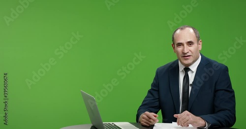 Positive male newsanchor reporting on current events. Happy man wearing a suit telling good news, shot on green chroma key background 4k footage photo