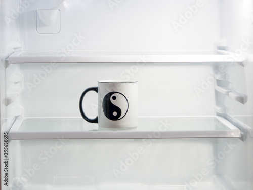 A Ying and Yang cup inside a white lighted refrigerator.